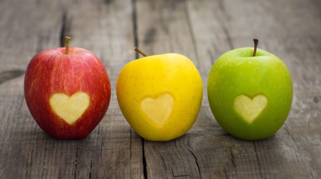 three apples with  engraved hearts on wood background
